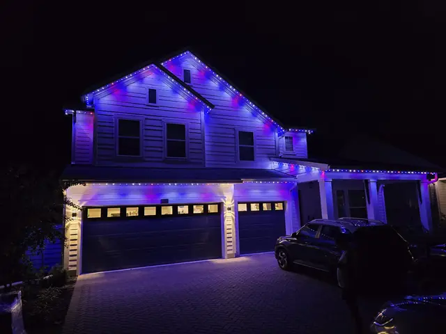 Two-story home with blue and purple roofline lights and white lights over the garage doors.