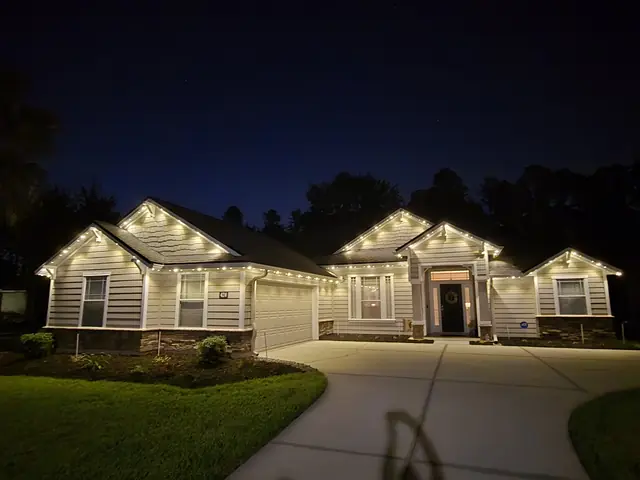 Single-story home with warm white lights along its gables and garage.