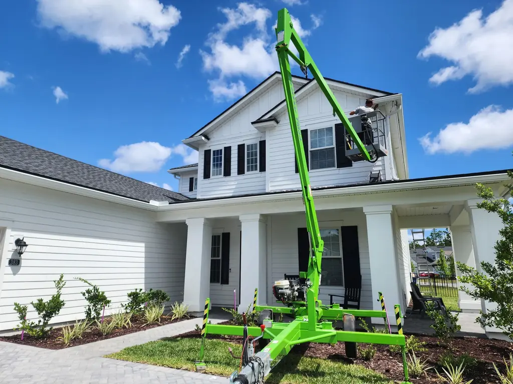 Glow Bug installer on an aerial lift working along the soffit of a two-story home in daylight.