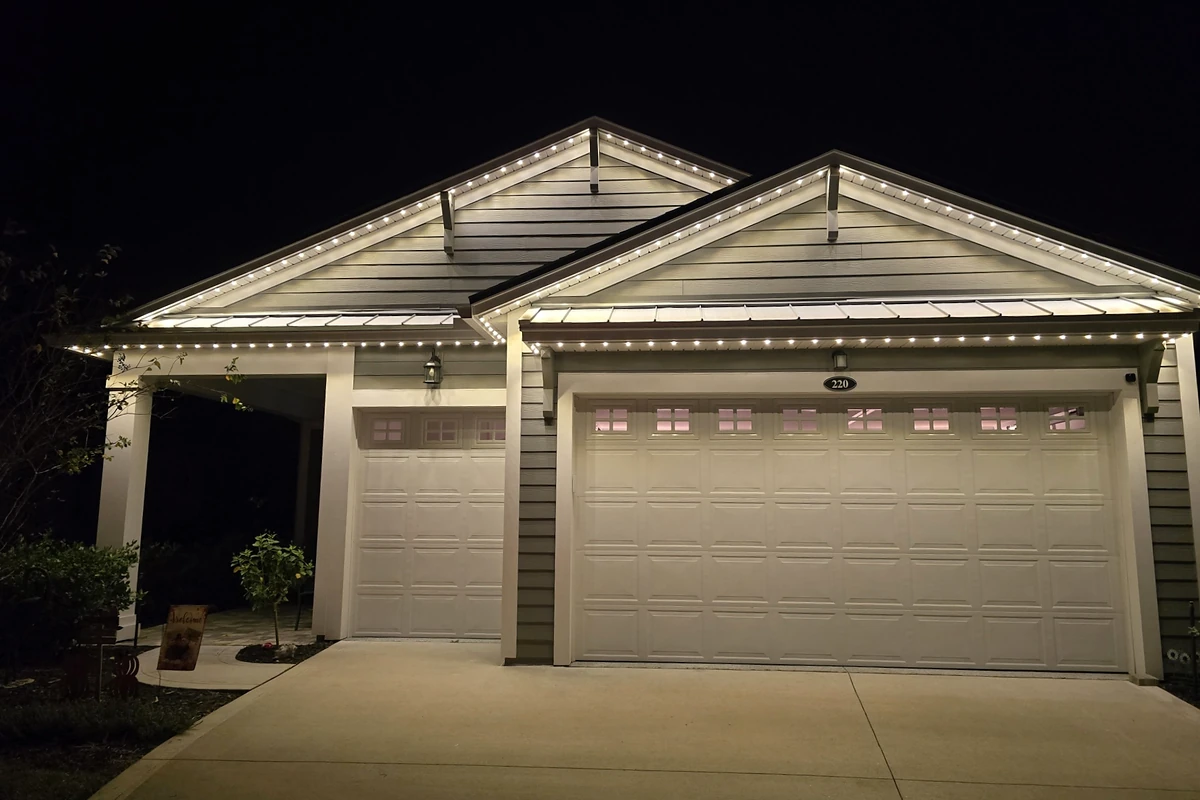 Home with warm white lights along the roofline above its garage.