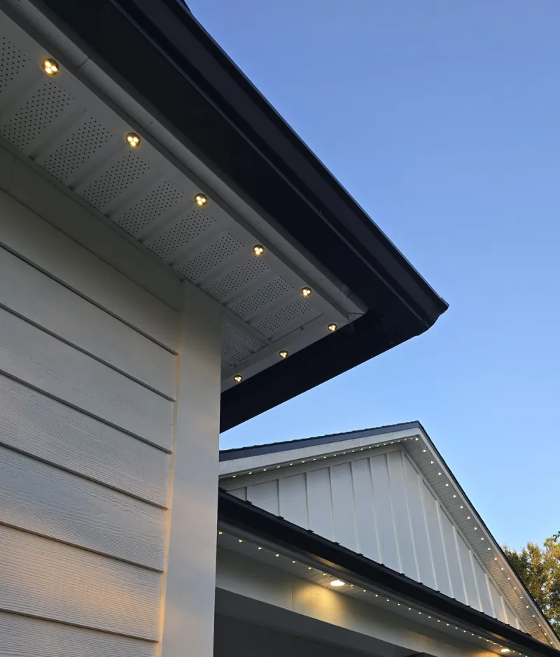 Warm lights follow a matching white track around a soffit corner in daylight.